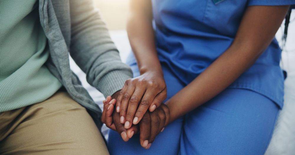 A caregiver holding hands with a senior patient in a hospital bed
