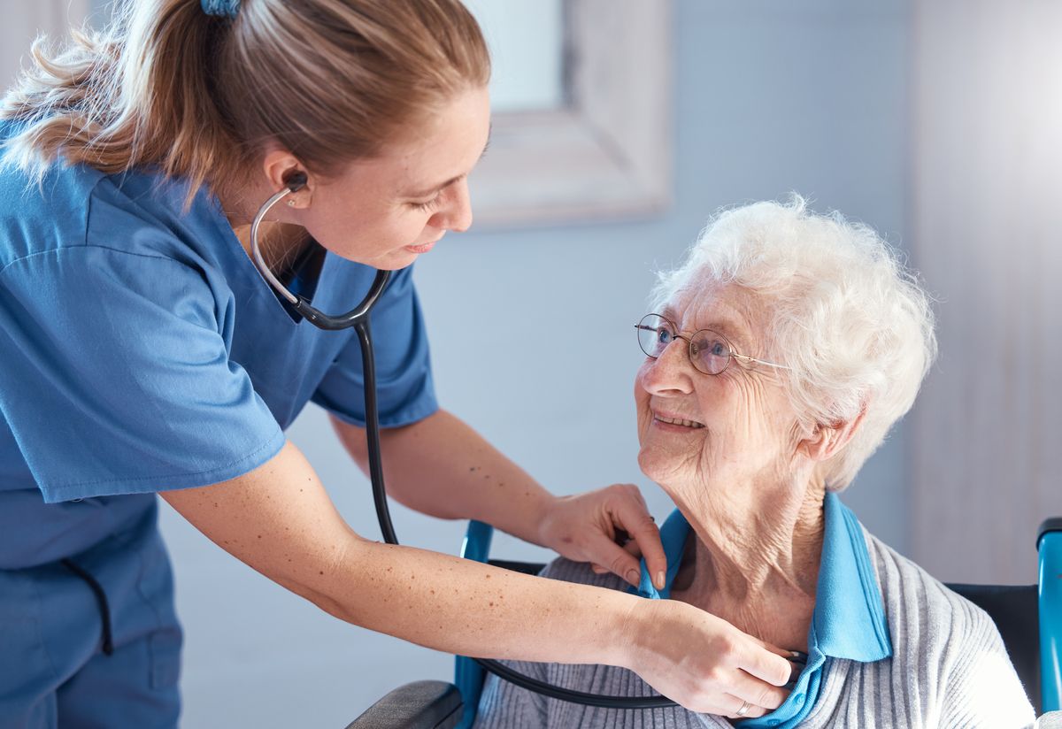 A nurse checking an elderly patient's heartbeat with a stethoscope